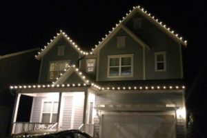 House illuminated with warm white Christmas lights along the roofline, showcasing a professional Christmas light installation in Naperville IL. The dark night sky contrasts with the cozy glow.