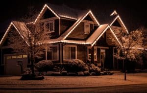 Home adorned with Christmas light installation. A cozy house glows with warm lights outlining the roofline against a snowy night, creating a festive winter scene.
