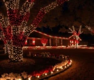 House beautifully decorated for Christmas with red and white lights outlining the roof, bushes, and trees. A homeowner in Naperville, IL could hire Christmas light installers like this to achieve a similar festive look.