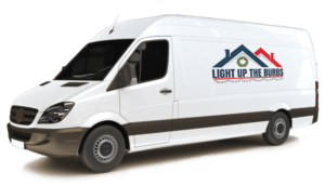 A white van with the "Light Up The Burbs" logo, specializing in Christmas light installation, is parked against a transparent background. The logo features a house silhouette with a festive wreath.