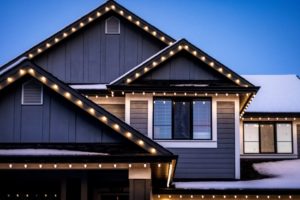 Home featuring Christmas light installation along the roofline of a gray house at dusk, with snow on the roof and ground.