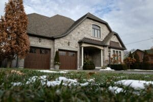 Suburban home with stone facade, brown garage doors, and hints of winter snow on the green lawn. A project for DIY home curb appeal to make your property standout.