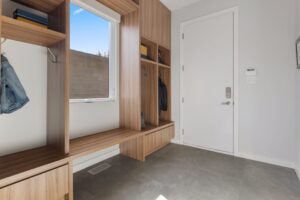 Modern mudroom with custom wood built-ins, gray tile floor, and a bright window. Functional home entry design with storage for coats, shoes, and bags.