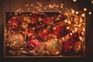 Festive holiday scene: red and gold Christmas ornaments nestled in a box, illuminated by twinkling fairy lights. Thinking about "are fairy lights a fire hazard" this holiday season?