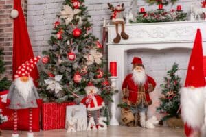 Festive Christmas scene with decorated tree, Santa figurine, gnomes, and gifts. "XMAS" block letters and a white mantle complete the cozy holiday display. Perfect for choosing a Christmas color palette.