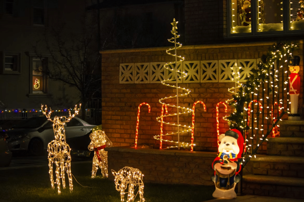 Outdoor Christmas light decoration ideas: A brick house glows with holiday cheer, showcasing illuminated deer, candy canes, spiral Christmas trees, and a toy soldier, creating a festive neighborhood scene.