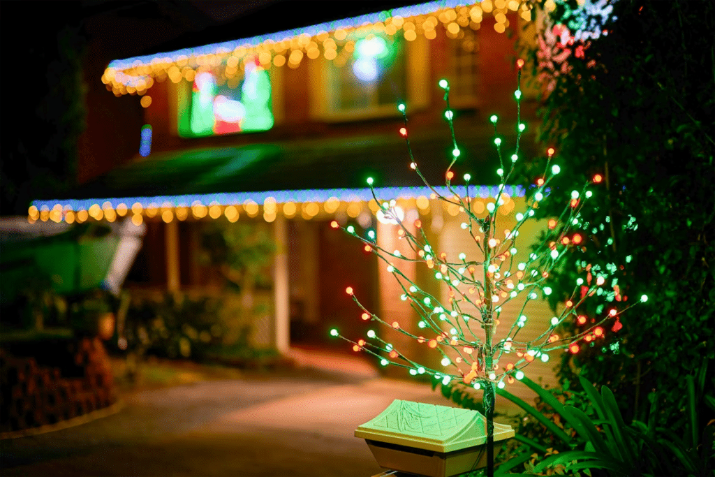 A home adorned with festive Christmas lights, showcasing how to hang Christmas lights on gutters. A small, lighted tree sits in the foreground, with the house's illuminated eaves and windows creating a warm, holiday glow.
